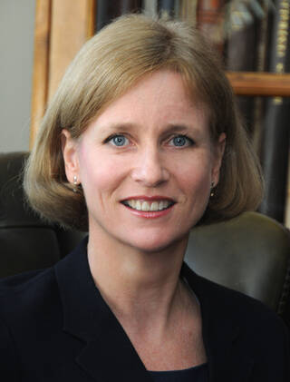 Colour photograph of the head and shoulders of a woman with blonde hair wearing black jacket.